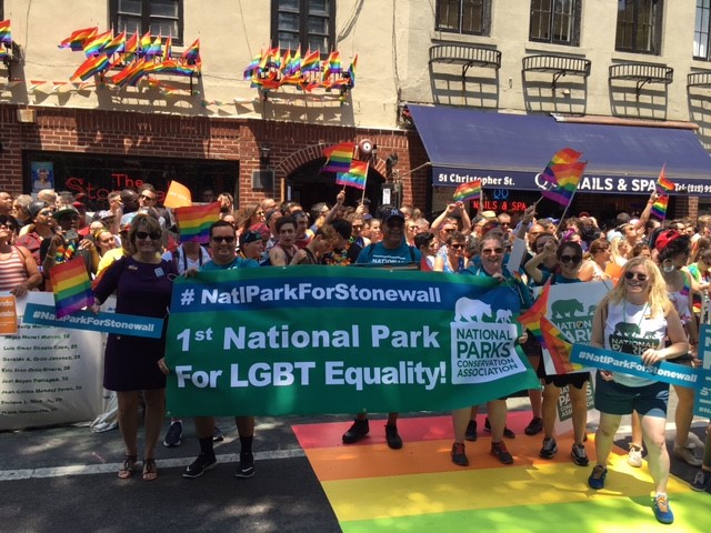 A photograph shows a group of people standing in front of the Stonewall Inn. At the front of the group, several people hold a banner that reads "1st National Park for LGBT Equality" and includes the NCPA logo.