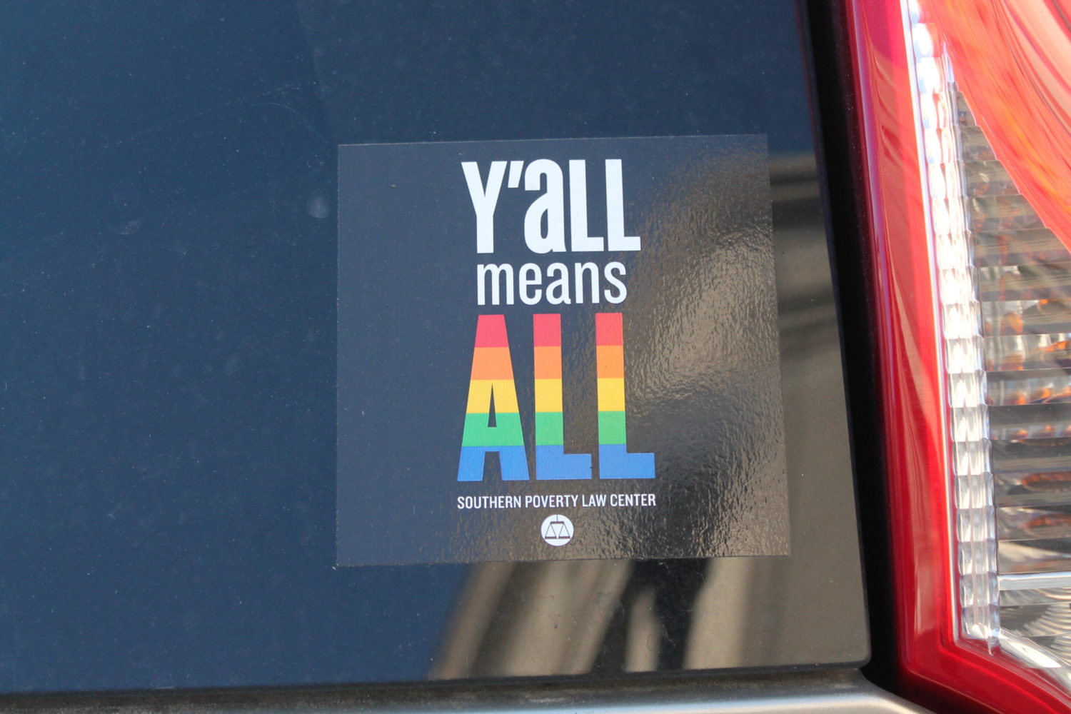 An image shows a sticker in the back of the car with the text "Y'all means all." The word "all" appears in rainbow colors.