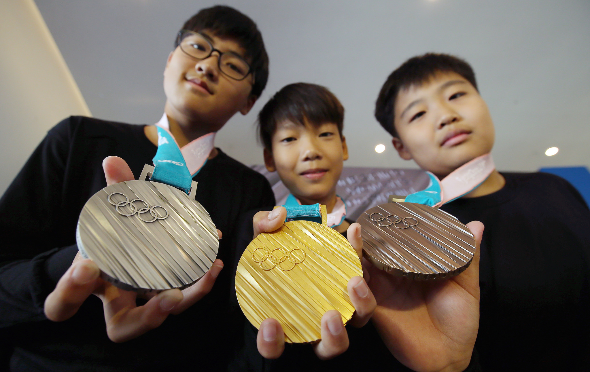 A photograph shows three young people holding a silver, gold, and bronze medal. 