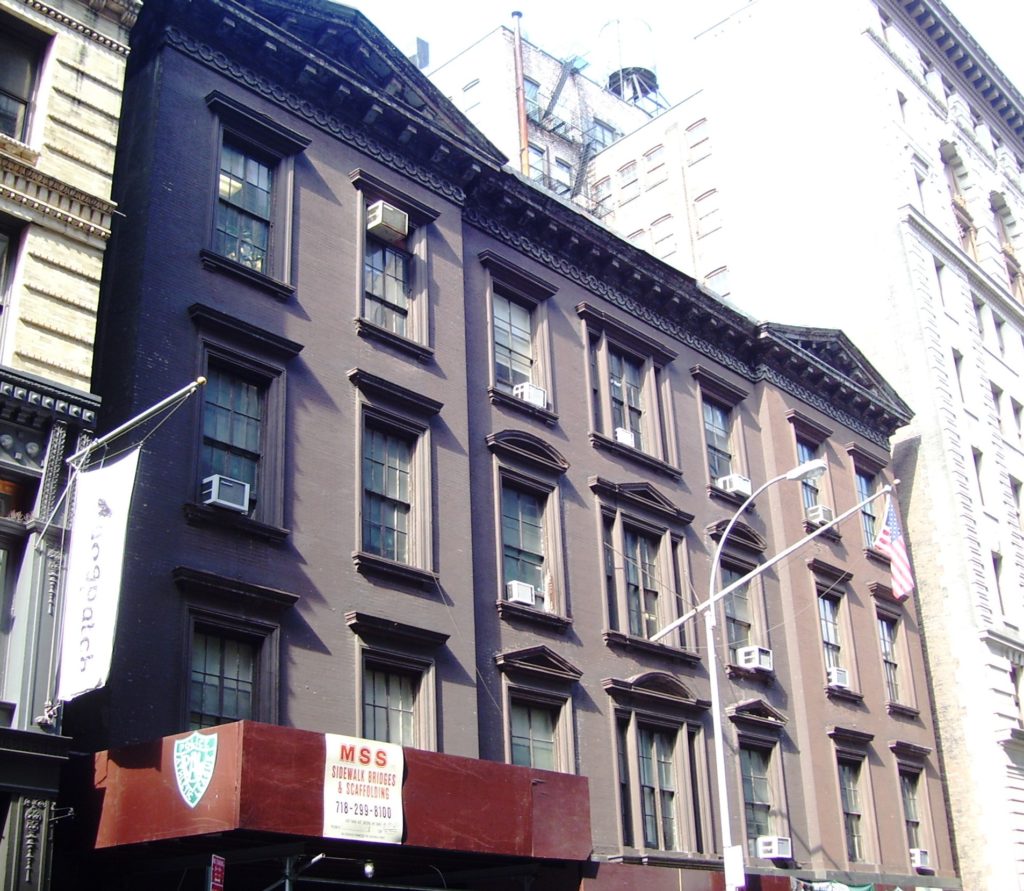 A photograph displays the facade of a large brown building on a city street.
