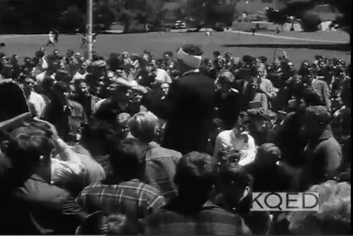 A man addresses a large crowd gathered around him.