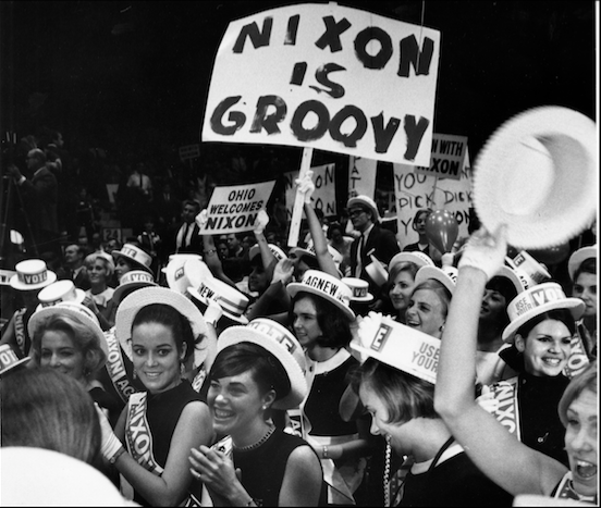 This image displays a crowd of smiling women wearing white hats that read "Vote" and sashes that read "Nixon." One woman holds a sign that reads "Nixon is Groovy" above the heads of the other women.