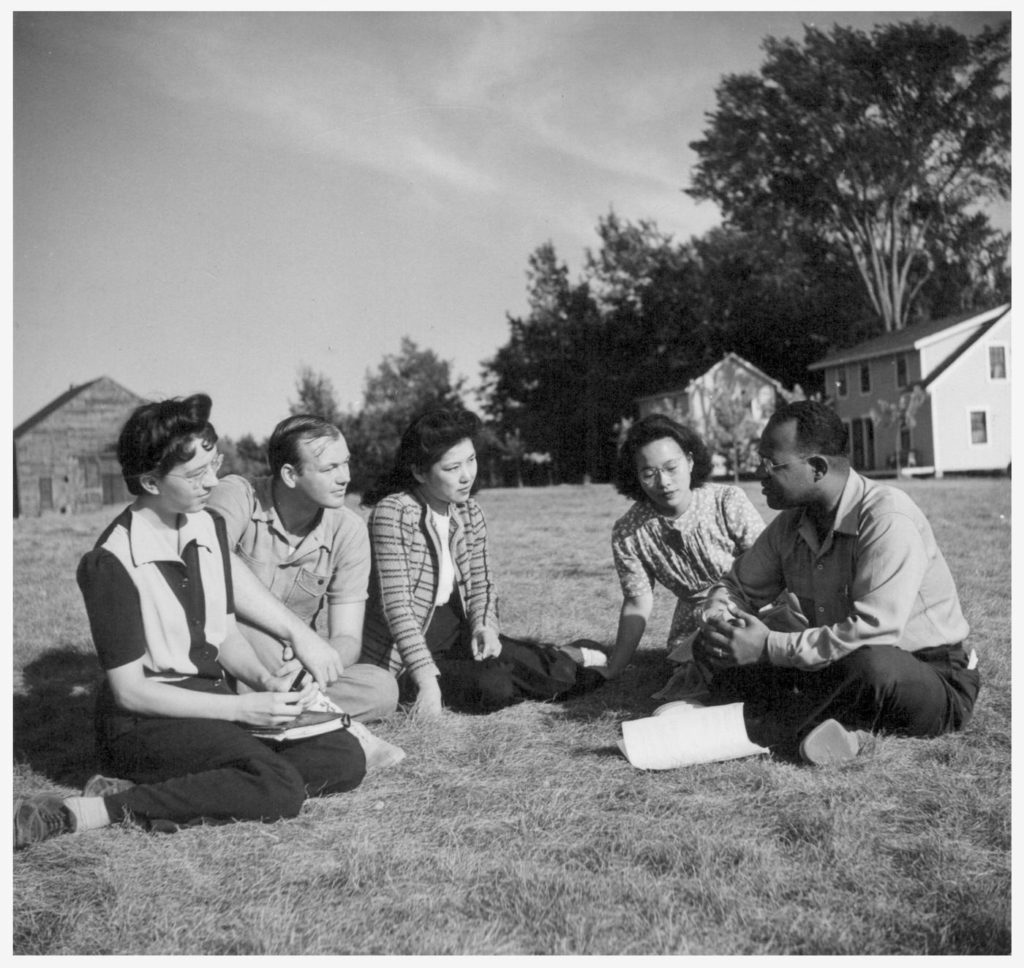 Five students of different races converse on a grassy field.